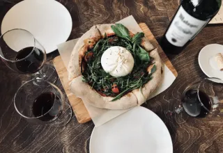 Pizza con burrata e rucola servita con calici di vino rosso