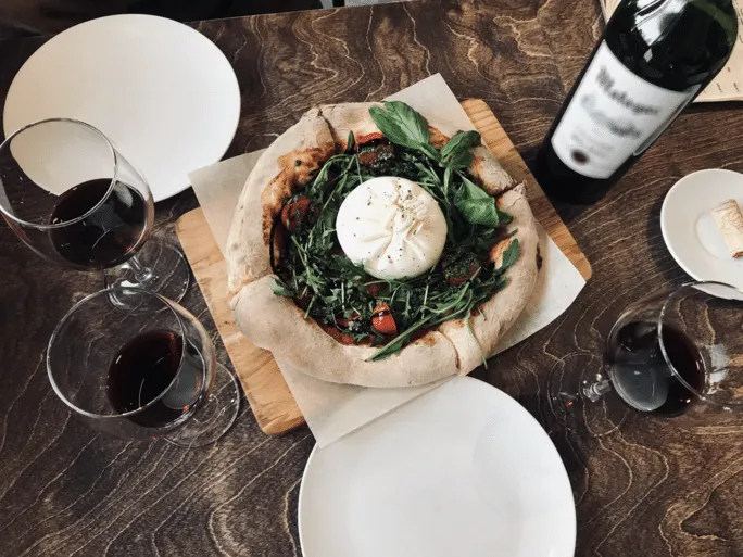Pizza con burrata e rucola servita con calici di vino rosso